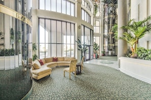 Eine geräumige Lobby mit einer gebogenen Couch, Sesseln und einem Couchtisch. Große Fenster und eine hohe Decke sind sichtbar.