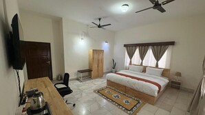Habitación de hotel con cama, escritorio, sillas, ventiladores de techo y televisión.