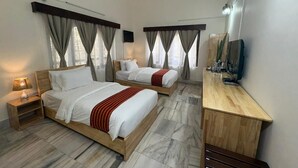 Una habitación de hotel con dos camas, un escritorio de madera, un ventilador de techo y un televisor.