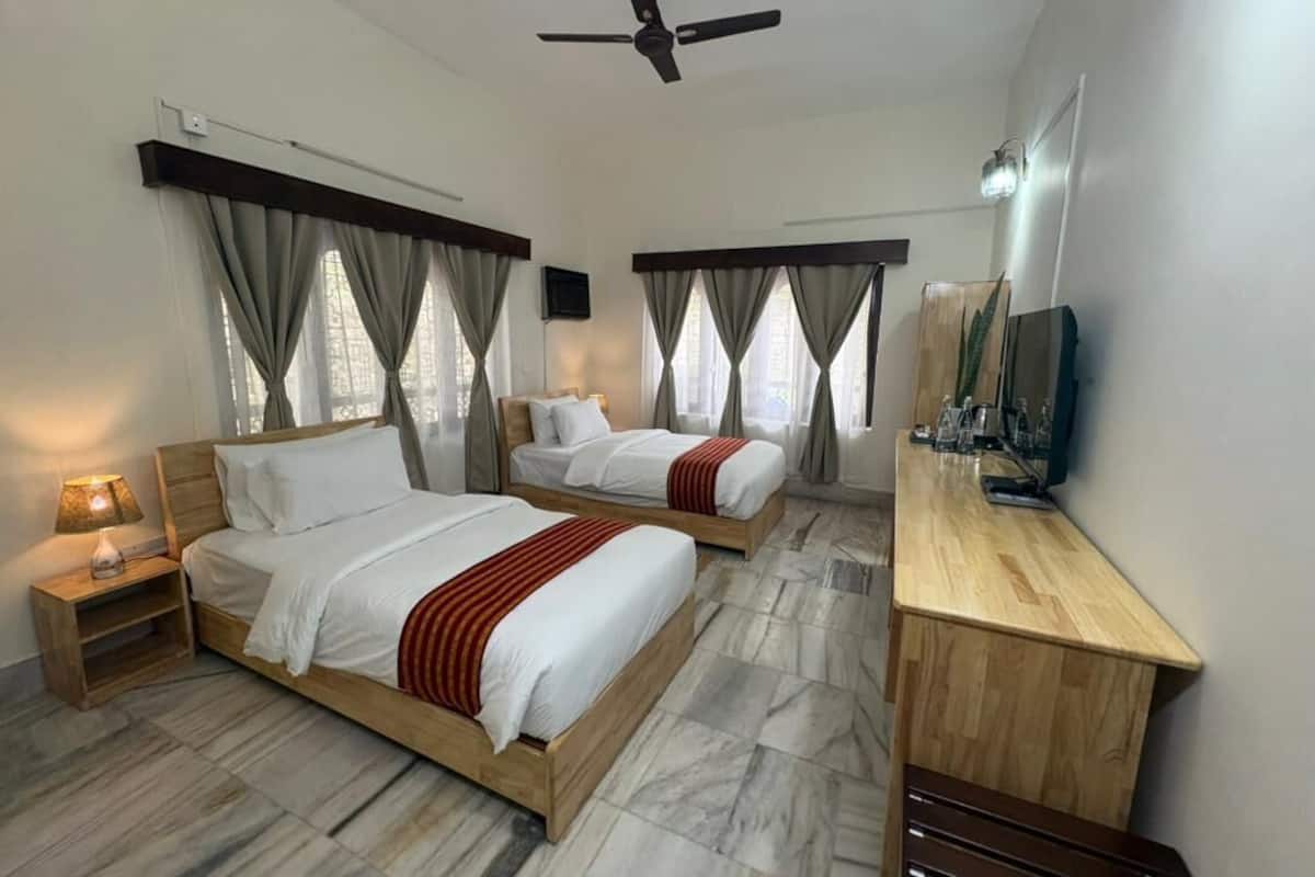 Una habitación de hotel con dos camas, un escritorio de madera, un ventilador de techo y un televisor.