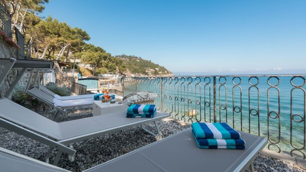 Una terraza frente al mar con sillones, una pequeña mesa y vistas al océano.