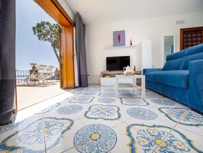 A living room with a blue sofa, a TV, and a patterned floor. - Casa Giovanna B in Nerano (Massa Lubrense)