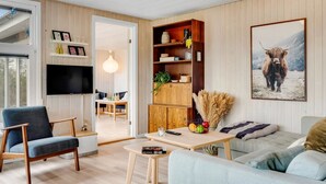 Una sala moderna con un sofá, una silla azul, una mesa de centro de madera y una estantería.