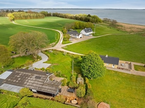 An aerial view of a property with a large green field, a house, a barn, and a body of water in the background. - "Brunetta" - 200m to the fjord by Interhome (Øster Assels)