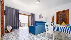 Une pièce avec un canapé bleu, une table à manger recouverte d’une nappe à rayures bleues et blanches, et des carreaux de sol à motifs.