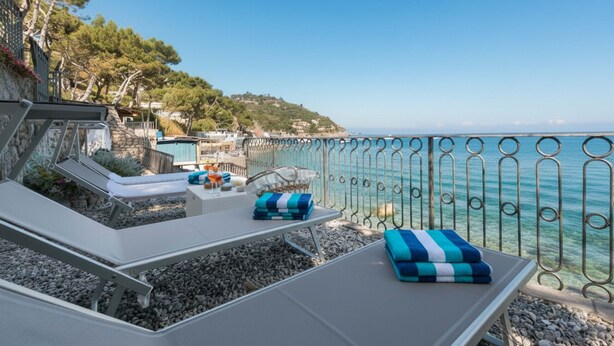 Un salon de bord de mer offrant une vue sur l’océan, avec un mur en pierre et une rambarde en métal.