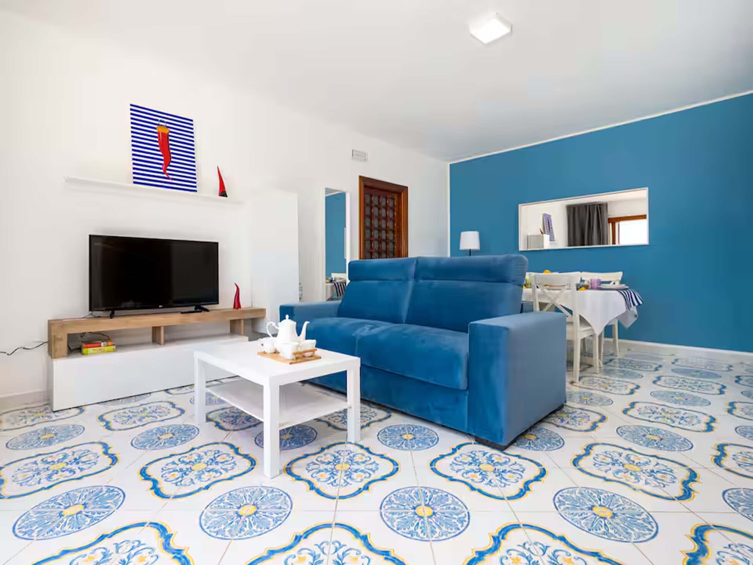 Een woonkamer met een blauwe bank, een flatscreen-tv, een salontafel en een vloer met een patroon.
