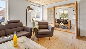 Una sala de estar moderna con techo de madera, dos sofás, una mesa de centro y un comedor con sillas y una mesa.