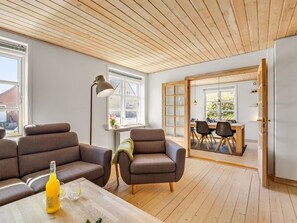 En moderne stue med træloft, to sofaer, et sofabord og et spiseområde med stole og bord.