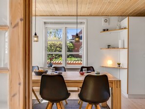 Et spiseområde med et træbord, sorte stole og et vindue med udsigt til grønne omgivelser.