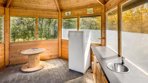 Una cabaña de madera con zona de cocina, que incluye un refrigerador, un lavabo y una mesa.