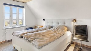 Un dormitorio con cama, mesita de noche, lámpara y ventana.
