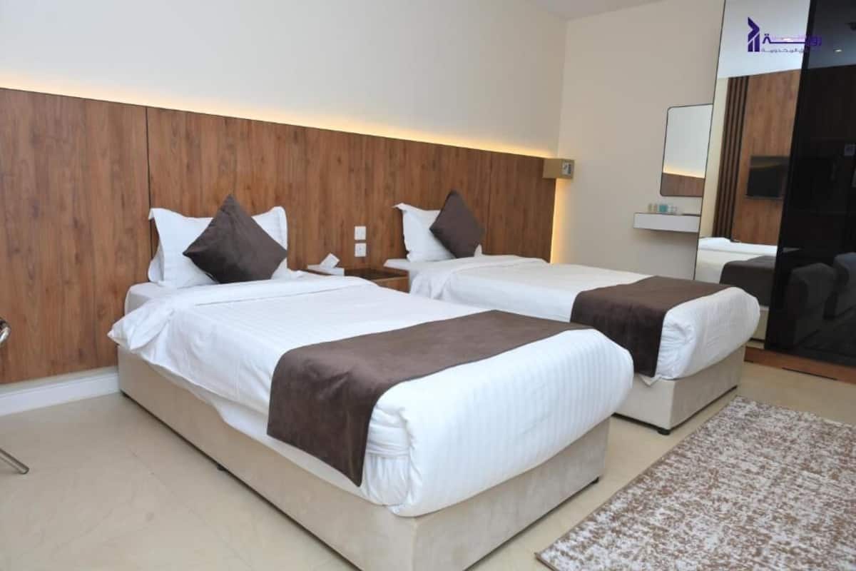 Habitación de hotel con dos camas, cabecera de madera, mesitas de noche y un espejo.