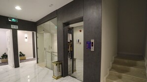 Un moderno vestíbulo de hotel con piso de mármol, un ascensor de vidrio y una escalera.