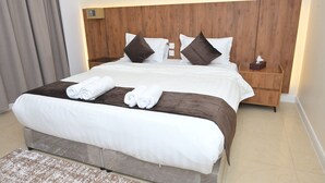 Una habitación de hotel con una cama grande, cabecera de madera, dos mesitas de noche y una mesita auxiliar.