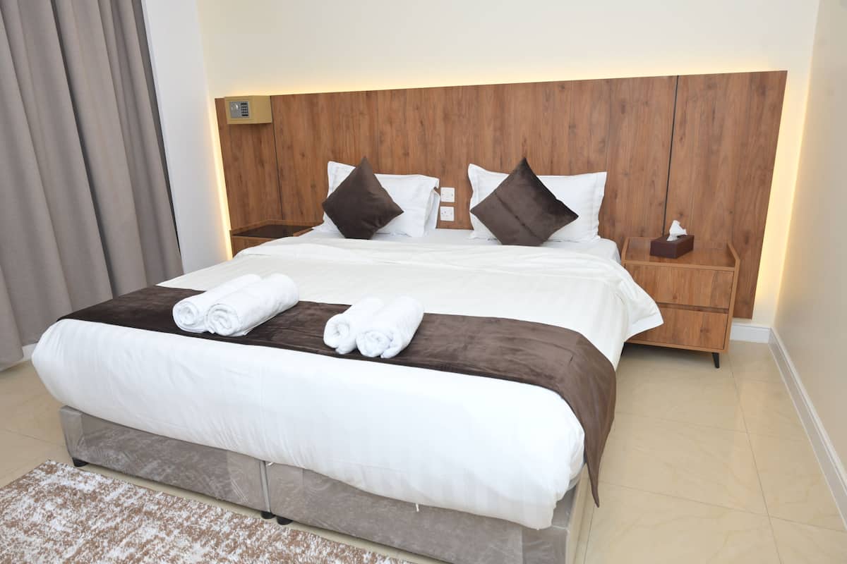 Una habitación de hotel con una cama grande, cabecera de madera, dos mesitas de noche y una mesita auxiliar.