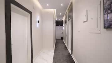 Un couloir aux murs blancs, aux moulures sombres et au sol en marbre, qui mène à une porte.
