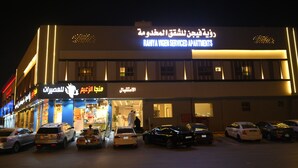 Un edificio con un letrero que dice 'RANYA VIGEN SERVICED APARTMENTS' y un estacionamiento con varios autos.