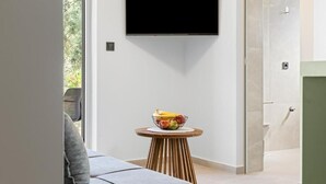 Una camera moderna con TV a schermo piatto montata a parete, un tavolino rotondo in legno con una ciotola di frutta e un divano grigio.