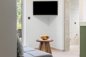 Ein modernes Zimmer mit einem an der Wand befestigten Flachbildfernseher, einem runden Holztisch mit Obstschale und einem grauen Sofa.