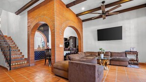 A living room with a brick archway, a brown sofa, a TV mounted on the wall, and a staircase with patterned tiles. - Private Boutique Hotel, Groups Up to 48 Guests (Puerto Vallarta)