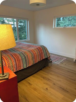 Ein Schlafzimmer mit einem Bett, einer Lampe, einem Teppich und zwei Fenstern.
