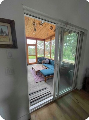 Ein Zimmer mit Holzboden, einem blauen Sofa, einem kleinen Tisch und Blick auf einen Wald durch große Fenster.