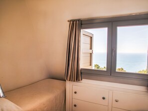 Habitació amb llit, una petita armari i finestra amb cortines.