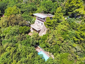 Un edifici modern i de diverses plantes envoltat de vegetació abundant, amb una piscina visible i una zona de solàrium.