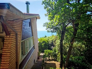 Ein Gebäude mit Backsteinfassade, Schornstein und Blick auf einen üppigen Garten und Bäume.