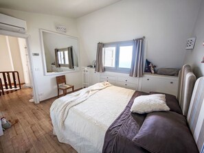 Ein Schlafzimmer mit Bett, Stuhl, Kommode, Spiegel und einem Fenster mit Vorhängen.