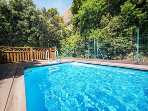 Una piscina amb terrassa de fusta i baranes de metall, envoltada d'arbres i una tanca.