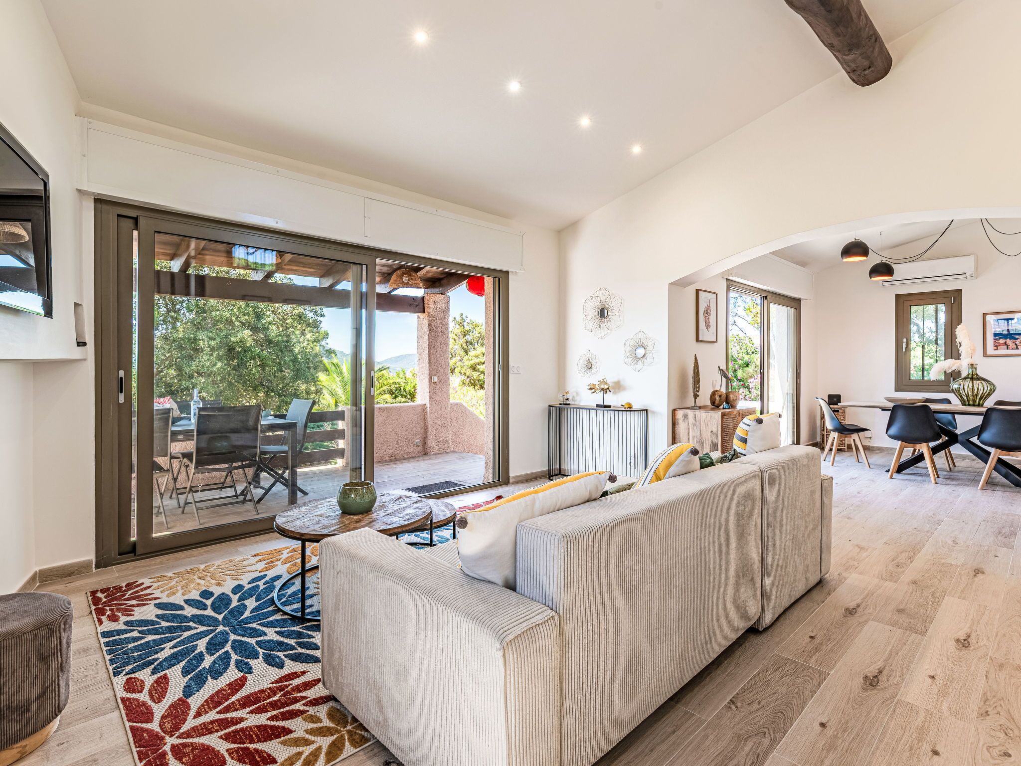 A modern living room with a sofa, a dining area, and a sliding glass door leading to an outdoor patio.