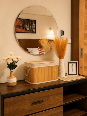 Une commode en bois avec un miroir, un vase de fleurs, un tableau encadré et une lampe.