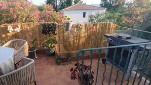 Eine Terrasse mit Tisch und Stühlen, einem Grill und einem Holzzaun mit Kübelpflanzen.
