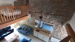 Ein Loft-Zimmer mit Holzbalkon, Steinwand, Sofa, Esstisch und einer Pendelleuchte.