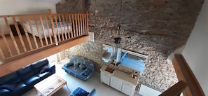 Ein Loft-Zimmer mit Holzbalkon, Steinwand, Sofa, Esstisch und einer Pendelleuchte.