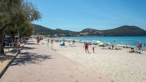 Ein Strand mit Menschen, Sonnenschirmen und blauem Himmel.