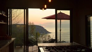 Una habitación con vista al mar, una mesa, sillas y un paraguas rojo.