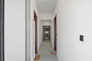 A narrow hallway with white walls, wooden doors, and a light-colored floor. - Robin's | White apartment (Lefkada)