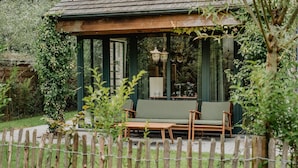 Un'area relax all'aperto, coperta, con un tavolo di legno e due sedie, circondata da un recinto in legno e vegetazione.