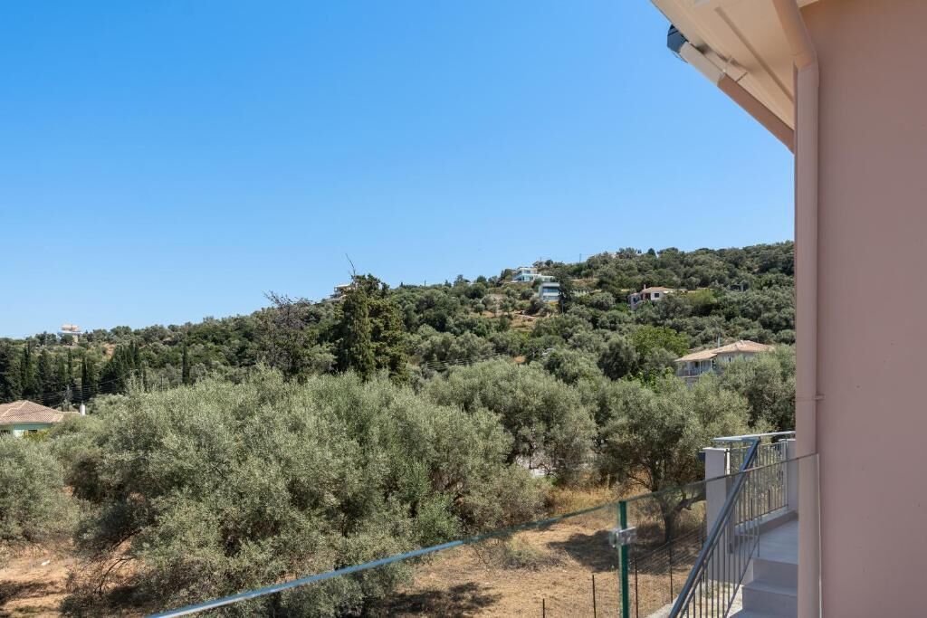 A balcony with a view of olive trees and houses on a hillside.