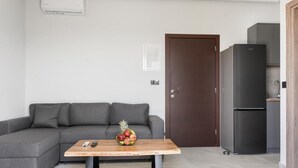 En moderne stue med en grå sofa, et træsofabord med frugt, en mørk dør og et sort køleskab.