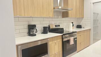 A modern kitchen with wooden cabinets, a stainless steel oven, a microwave, a coffee maker, and a toaster.