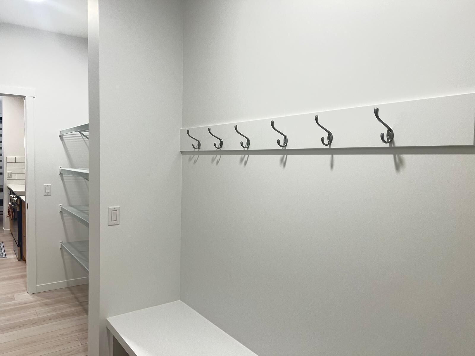 Ein Flur mit weißer Wand, einem Metallgestell mit Haken und einer weißen Bank.