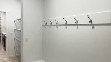 Ein Flur mit weißer Wand, einem Metallgestell mit Haken und einer weißen Bank.