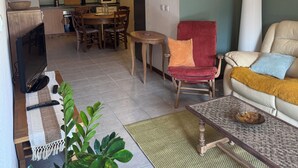 A living room with a television, sofa, and armchair, a dining area with a table and chairs, and a kitchen with a microwave and cabinets. - Cosy apartment under vaulted ceiling-6 people- Le Secret d'Adèle (Châteauroux-les-Alpes)