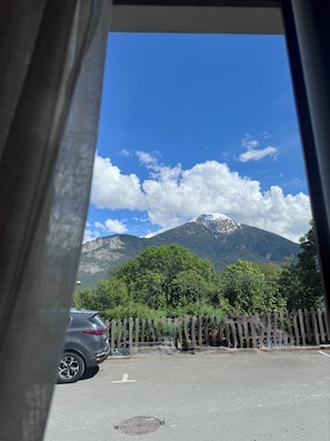 Bergblick durch ein Fenster, mit einem geparkten Auto und einem Holzzaun.