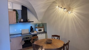 A compact kitchen with a dining table, wooden cabinets, a microwave, and a coffee maker. - Cosy apartment under vaulted ceiling-6 people- Le Secret d'Adèle (Châteauroux-les-Alpes)