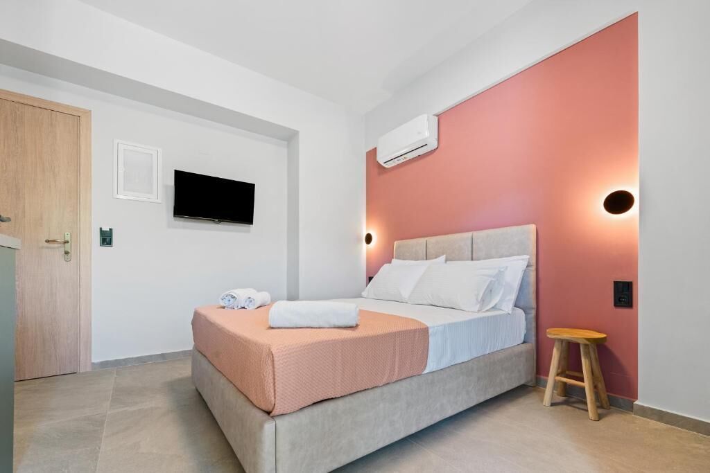 A bedroom with a bed, an air conditioning unit, a television, and a stool.